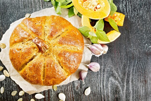 Pompoenbrood op perkament, knoflook, basilicum, plakjes en zaden van een groente op de achtergrond van een houten plank van bovenaf