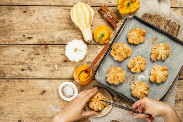 Pompoenbroodjes of koekjes, traditionele herfstgebakken goederen. vrouwelijke handen houden cookies vast. seizoensgebonden zelfgemaakte gerechten en herfstdecor. oude houten planken achtergrond, bovenaanzicht