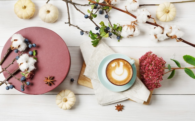 Pompoenkruid latte. Blauwe koffiekop met romig schuim, gedroogde herfstbloemen, sleedoorn en kleine gele pompoenen. Warme drank vallen en doos aanwezig