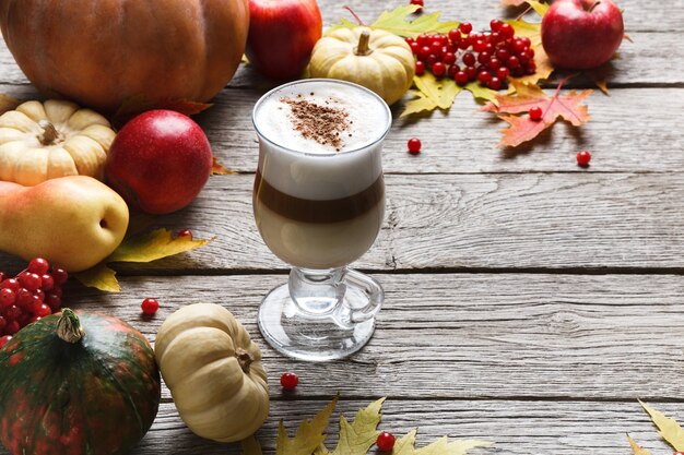 Pompoenkruid latte. glazen koffiekopje met romig schuim, gedroogde herfstbladeren, appels en kleine pompoenen op rustiek hout. herfst warme dranken, seizoensgebonden aanbod concept