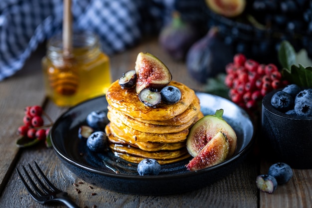 Pompoenpannenkoekjes met stroop of honing, lijnzaad, vijgen, bosbessen in een donkere plaat op tafel