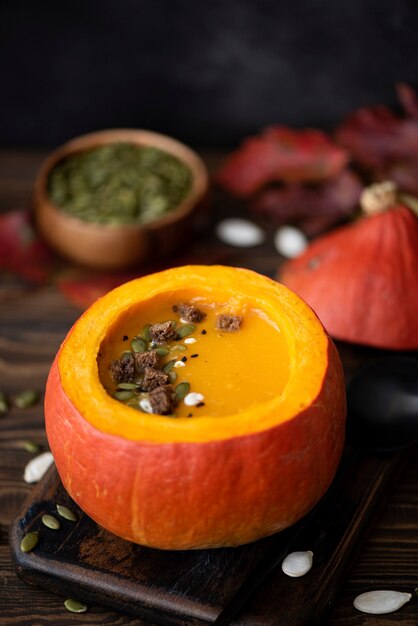 Pompoenpuree soep in pompoen met zaden en sesamzaadjes op een houten tafel