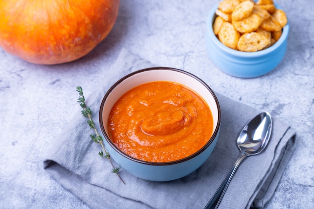 Pompoenroomsoep met croutons en tijm in een kom. Vegetarische huisgemaakte warme soep. Grijze achtergrond, close-up.