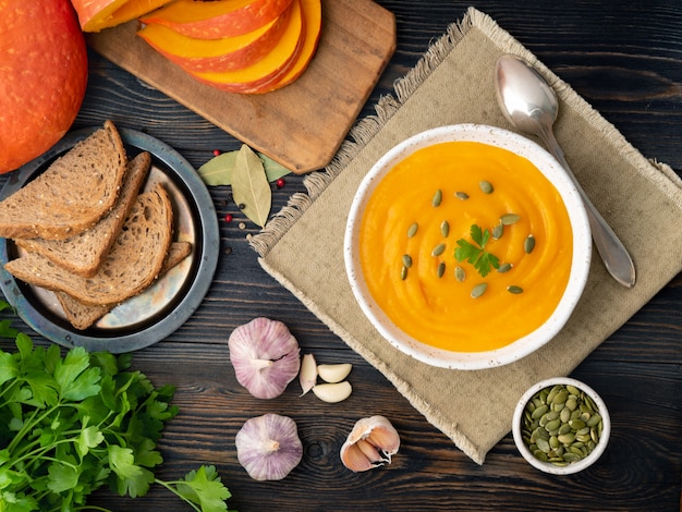 Pompoensoep fijngestampt in een witte plaat, pompoenpitten, brood, knoflook op donkere houten achtergrond