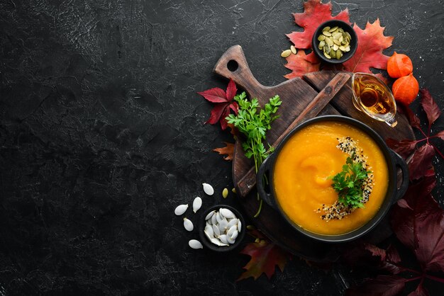 Pompoensoep met pompoen en gekleurde herfstbladeren plat op een zwarte stenen achtergrond Bovenaanzicht Vrije ruimte voor uw tekst