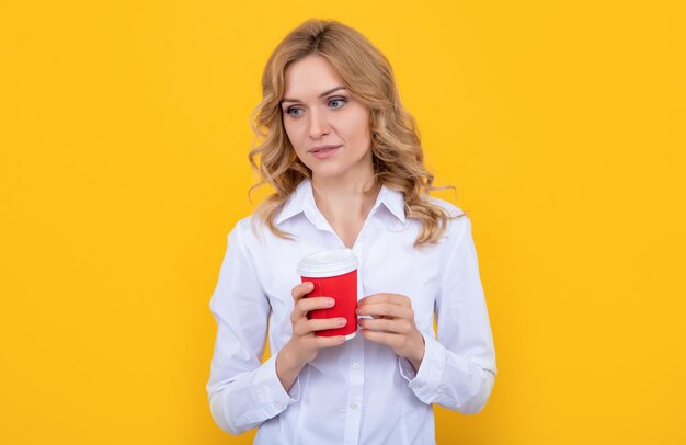 Pondering blonde woman with morning coffee cup on yellow background