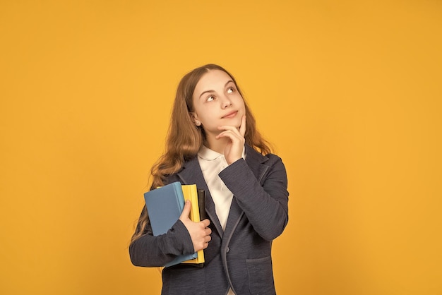 Pondering teen girl hold school workbook on yellow background homework