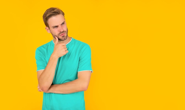 Pondering unshaven young man in blue shirt on yellow background lifestyle