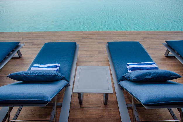 青いラウンジチェアと海の景色を望むテーブルを備えたプールデッキ。