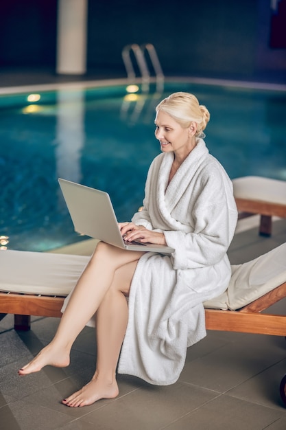 In a pool. Pretty woman in a white robe with a laptop in a swimming pool