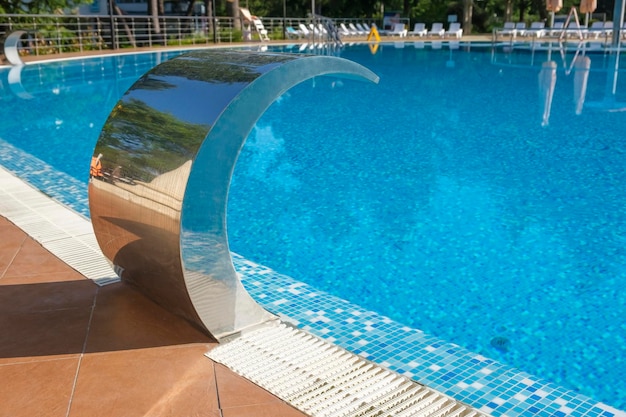 Pool side Empty outdoors swimming pool and waterfall jet on summer sunny day Seaside vacation and hotel resort concept Reflection in blue clean sea water pool