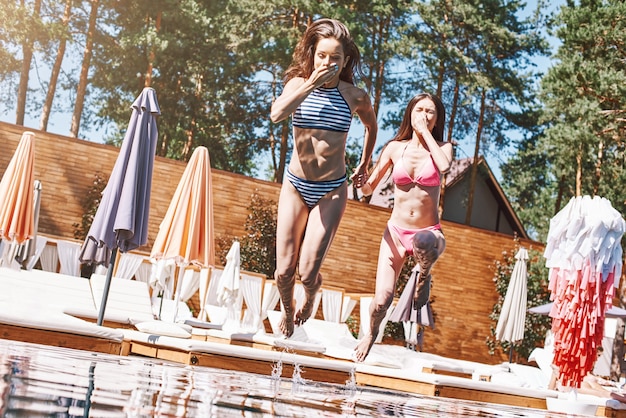 수영장 시간 수영장에서 점프하는 세련된 수영복을 입은 두 명의 아름답고 날씬한 젊은 여성