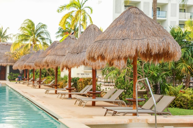 A pool with thatched umbrellas and a pool in front of a hotel.