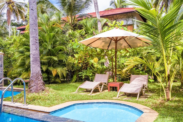 Pool with umbrella and beach beds in tropical hotel or residential house