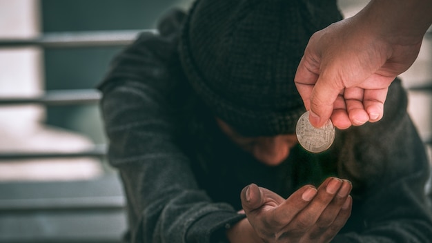 Poor homeless man or refugee sitting on on the dirty floor recieving money.