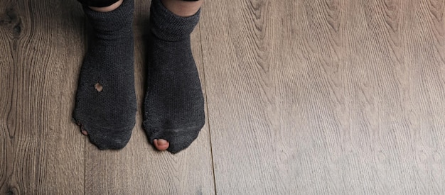 Poor person in shabby socks on wooden floor closeup view with space for text Banner design