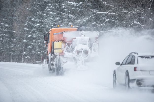 Photo poor road visibility of a car driving right behind a snow plow during winter road maintenance.