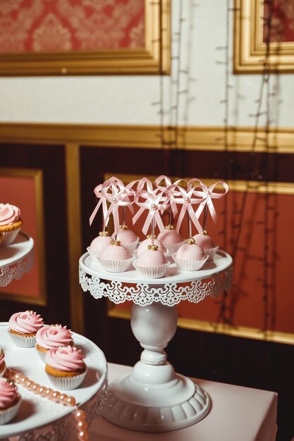 Foto torte pop con crema rosa e decorate con perle di pasticceria dorate su un vassoio bianco
