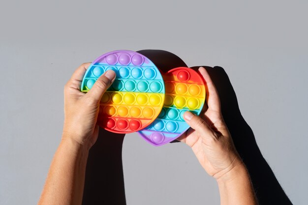 Pop it toy, someones hands with silicone toy in rainbow hues for relaxation