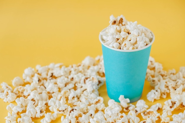 Popcorn in a blue paper cup on a yellow background. Minimalist concept. Copy, empty space for text.