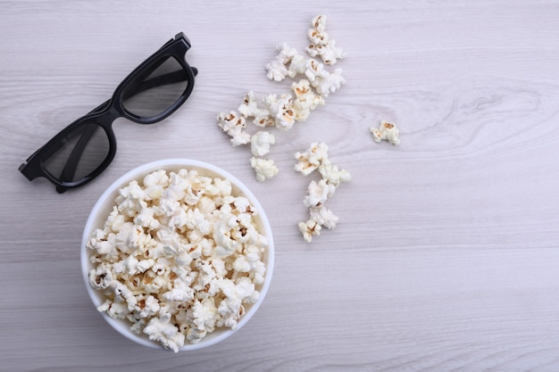 Popcorn in a bowl and 3D glasses on a light wooden