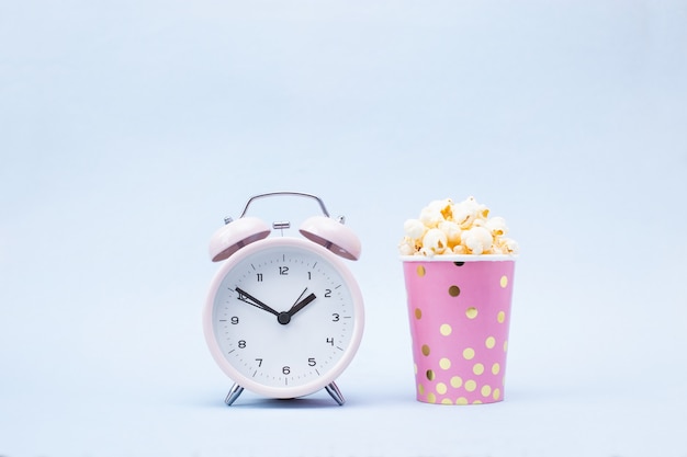 Popcorn in a bright glass and alarm clock on blue