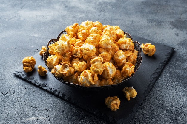 Popcorn in caramel glaze in a plate on a dark concrete table.