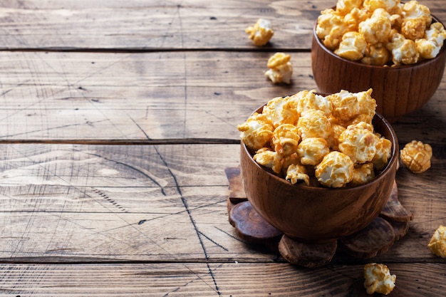 Popcorn nella glassa del caramello in piatti di legno su una tavola rustica.