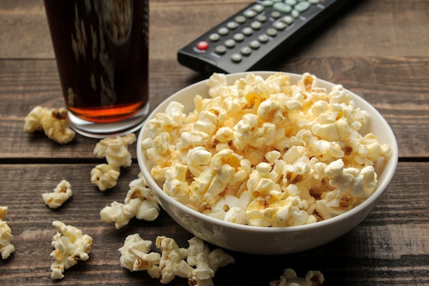 Popcorn, coca cola and TV remote on a brown wooden table, concept of watching movies at home.