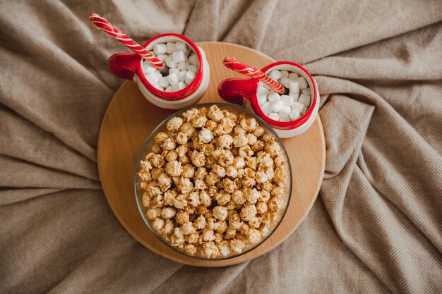 Popcorn in una ciotola di vetro e due tazze con marshmallow su una tavola di legno.