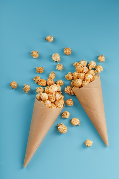 Popcorn in karamelglazuur in een papieren envelop op een blauw.