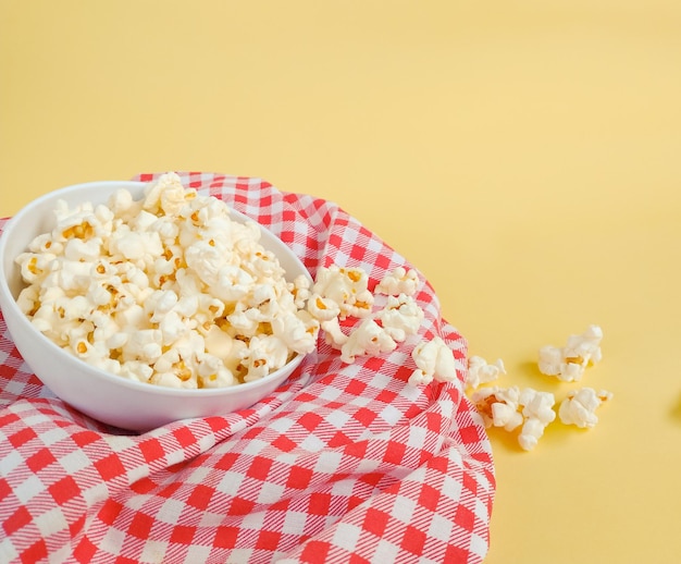 Popcorn in kom bovenop geruite doek op gele achtergrond