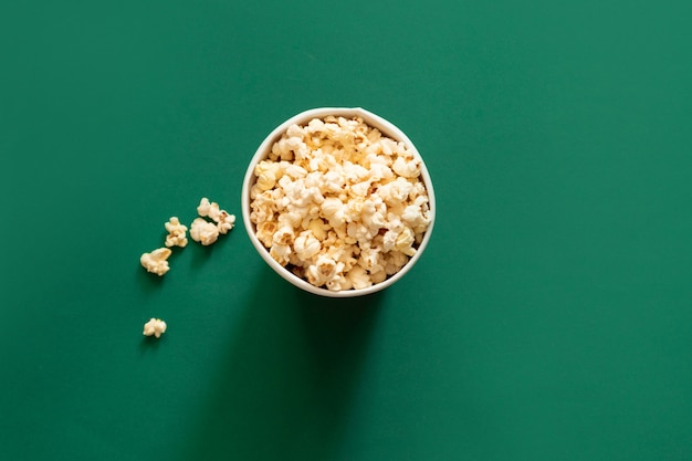 Popcorn in paper bag on green background. Unhealthy diet concept.