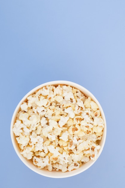 Popcorn in a paper cup is isolated on a pastel blue background, a view from above. Flat lay.