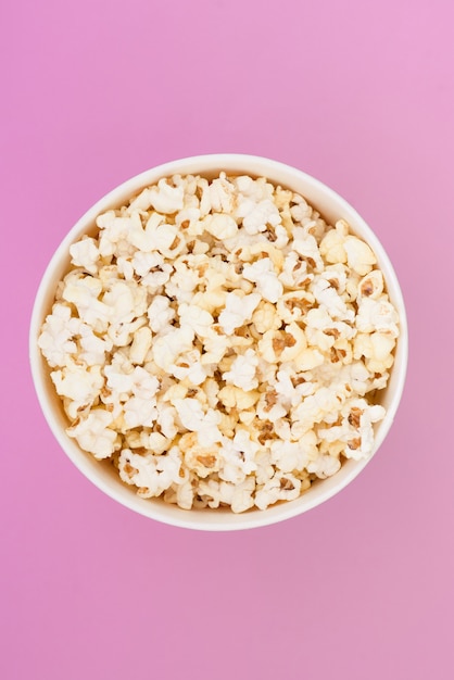 Popcorn in a paper cup is isolated on a pastel pink background, a view from above. Flat lay.