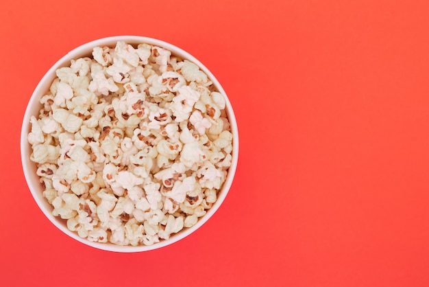 Popcorn in un bicchiere di carta è isolato su uno sfondo rosso, una vista dall'alto. disteso