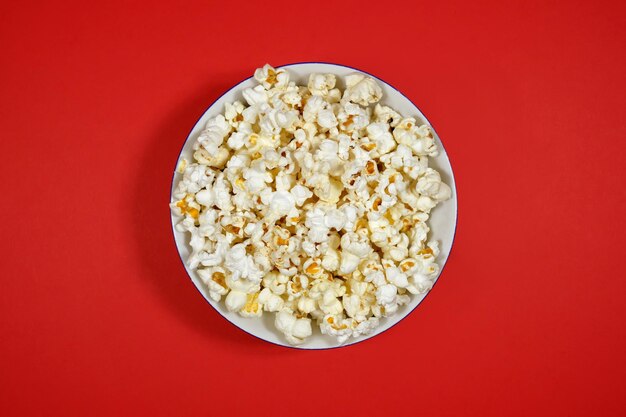 Popcorn in a plate on a red paper background closeup top view