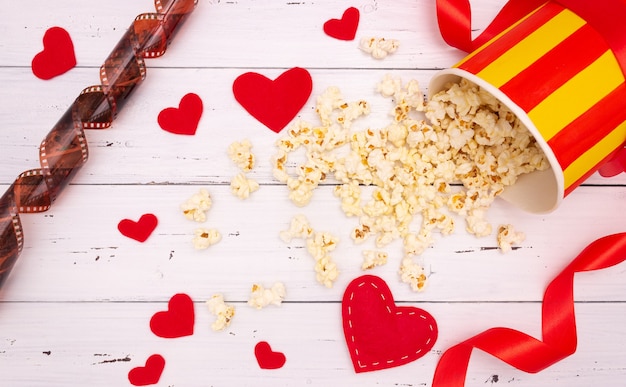 Popcorn, red hearts and ribbon on a white wooden background. valentine's day, movie theater.