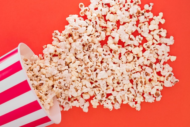 Popcorn rises from a paper bowl to a red background, a view from above.