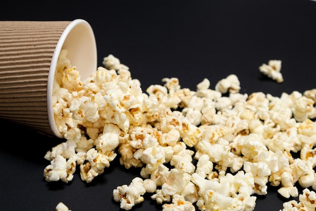 Popcorn spills out of a brown paper cup on a black background closeup