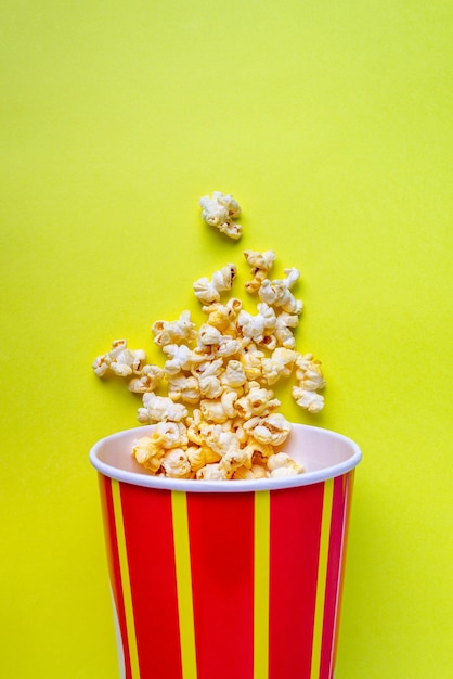 Popcorn stroomt uit een gestreepte papieren emmer op een gele achtergrondkopieerruimte