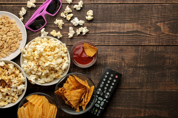 Popcorn e snack vari, occhiali 3d, telecomando tv su uno sfondo di legno marrone. concetto di guardare film a casa. vista dall'alto