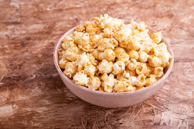 Popcorn with caramel in ceramic bowl on brown