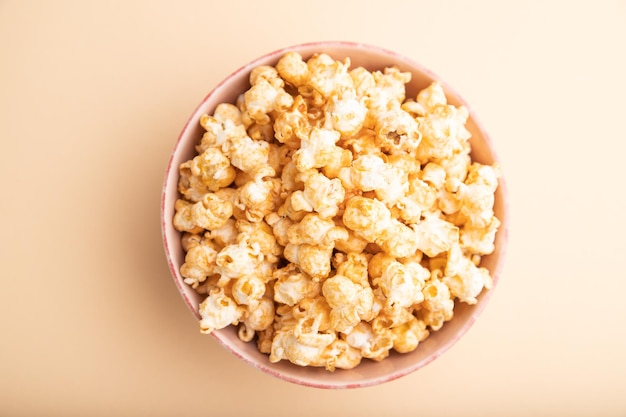 Popcorn with caramel in ceramic bowl on pastel orange background. Top view, flat lay, close up.