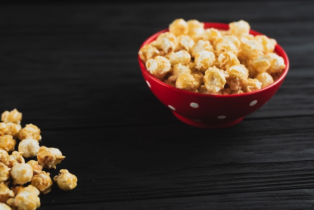 Popcorn with caramel in a red plate on a black wooden background scattered