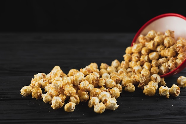 Popcorn with caramel in a red plate on a black wooden background scattered