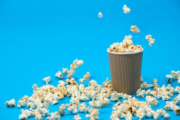 Popcorn wordt gegoten in een bruin papierglas op een blauwe achtergrond met plaats voor tekst