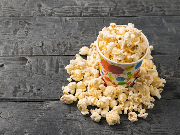 Popcorn wordt uit een veelkleurige papieren beker gegoten op een rustieke donkere tafel.