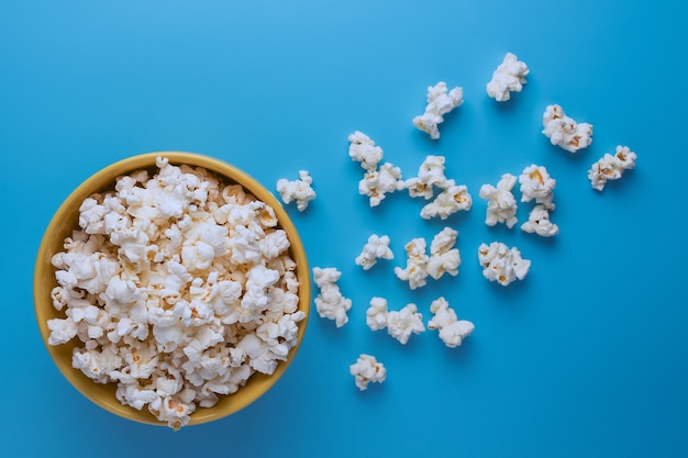 Popcorn in una tazza gialla su sfondo blu e popcorn sparsi nelle vicinanze