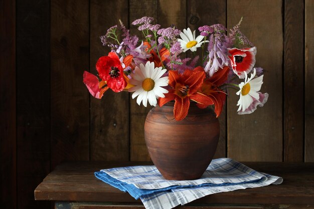 Poppies lilies daisies and yarrow Garden flowers in a clay jug